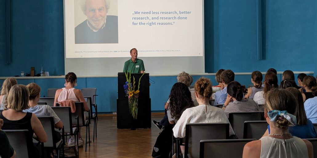 Prof. Dr. Jörg Meerpohl steht beim Methodenforum am Rednerpult und begrüßt die Teilnehmer*innen, die vor ihm sitzen. An der Wand hinter Meerpohl ist seine Präsentation zu sehen. Foto: CDS