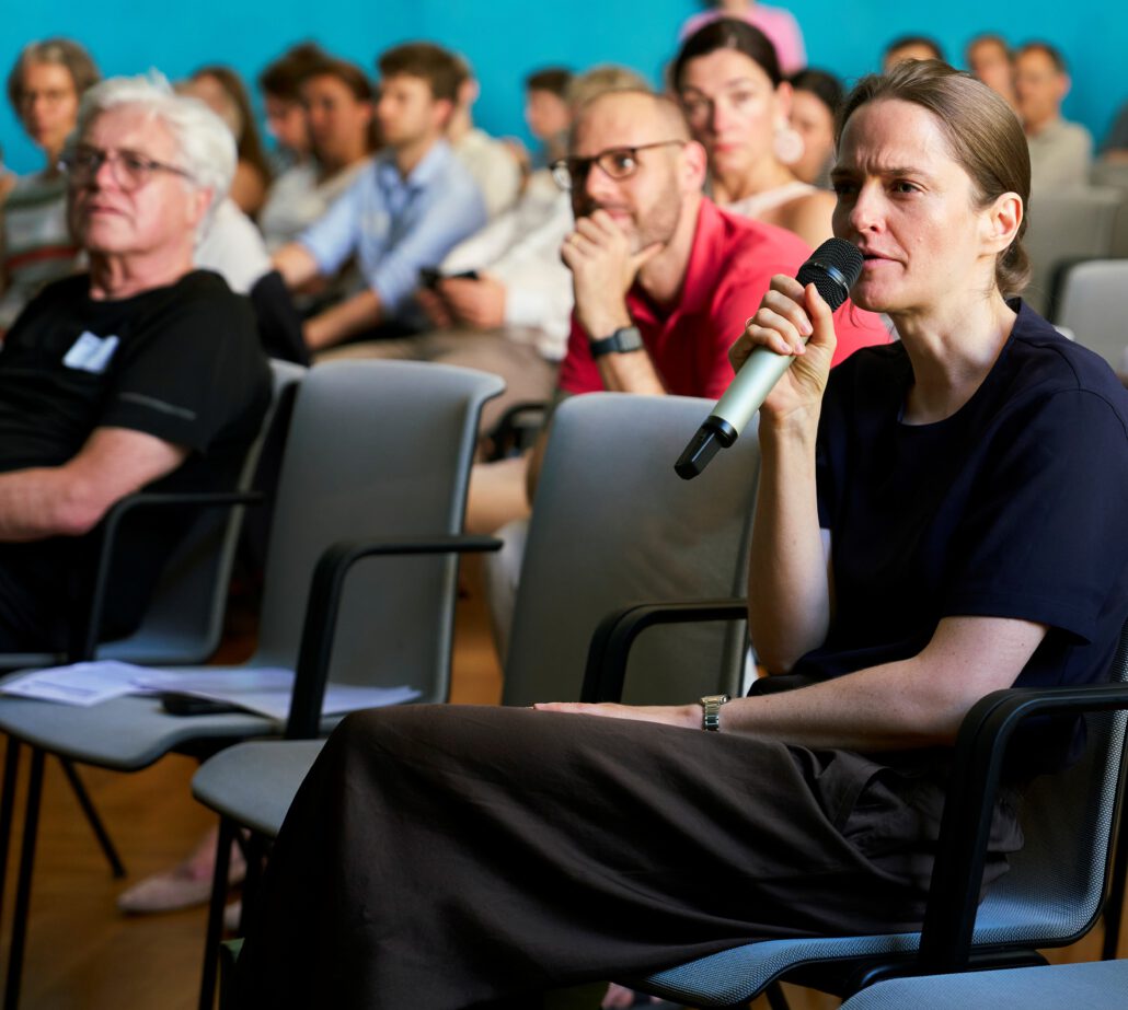 Claudia Breuer, stellvertretende Direktorin von Cochrane Deutschland, spricht beim Methodenforum ins Mikrofon. Im Hintergrund sitzen Teilnehmer*innen. Foto: CDS