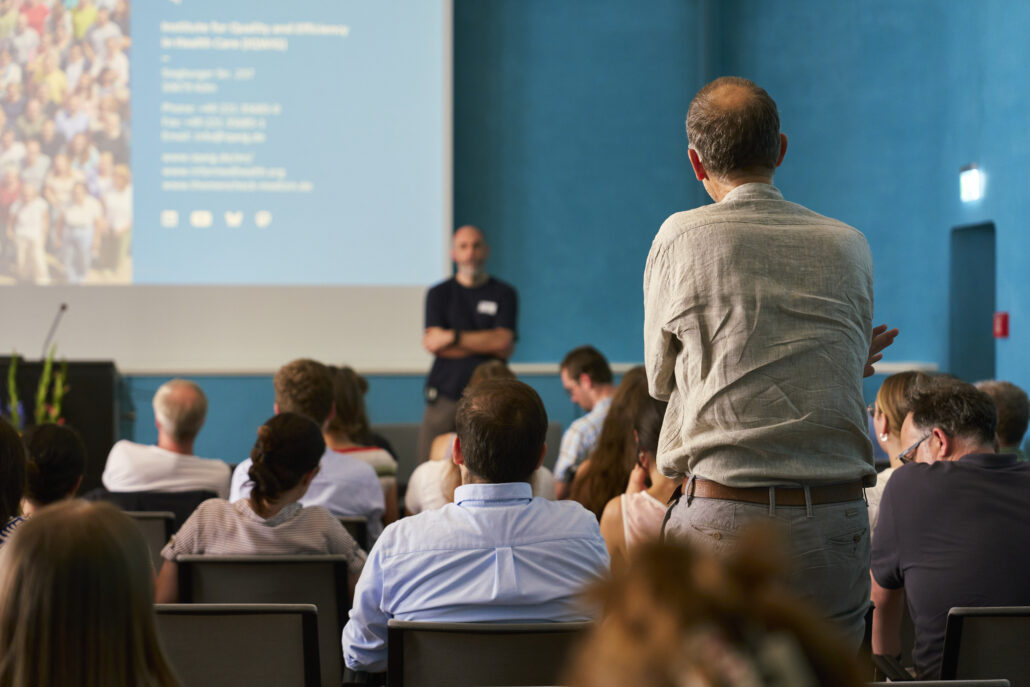 Zuhörer*innen beim Methodenforum 2026 der Cochrane Deutschland Stiftung, im Hintergrund steht unscharf Volker Vervölgyi. Foto: CDS