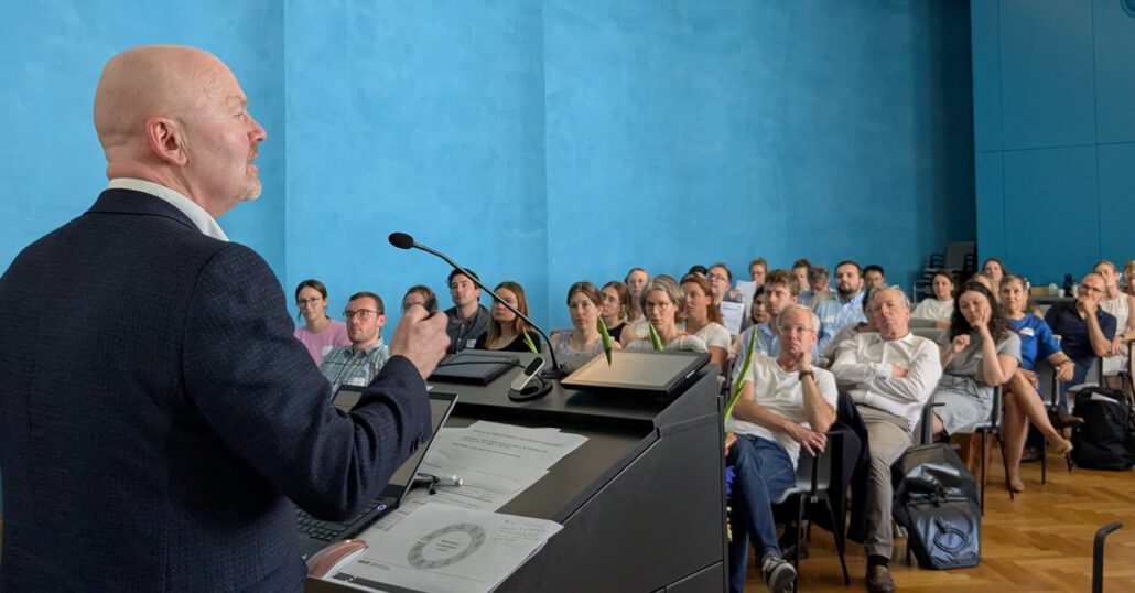 Dr. Gary Hickey spricht am Rednerpult ins Mikrofon. Vor ihm sitzen etliche Zuhörer*innen. Foto: CDS