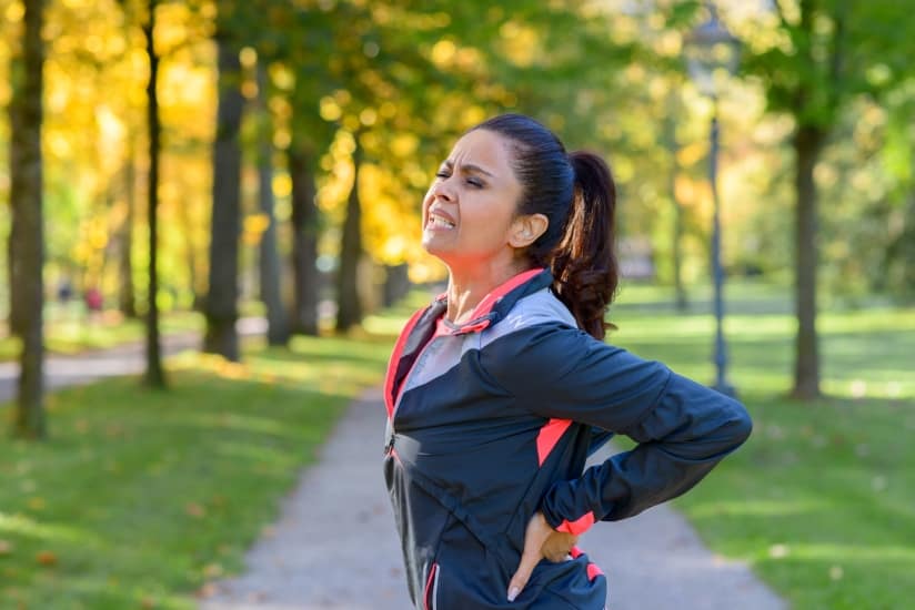 Adult woman holding her painful back after exercising in park